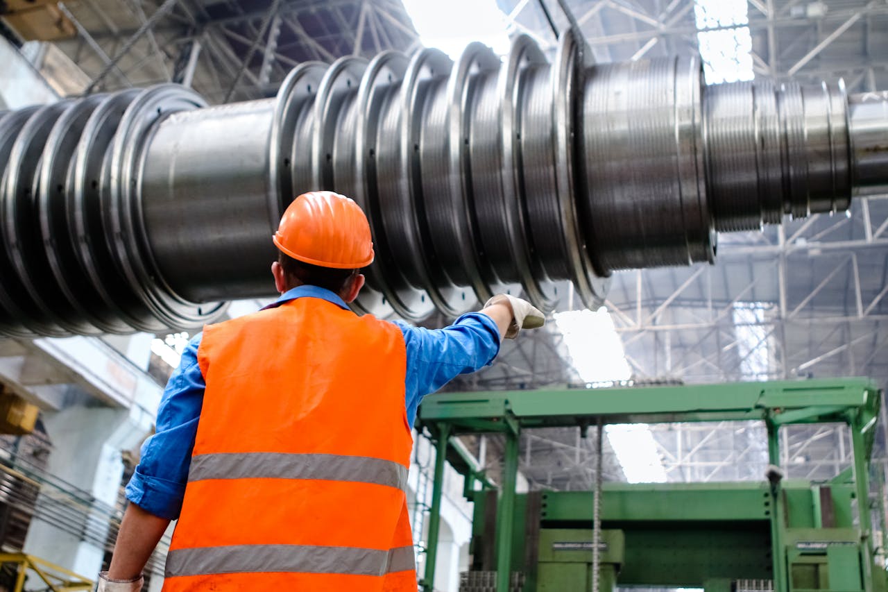 about-02 Engineer in high visibility vest and hard hat inspecting large machinery in factory setting.