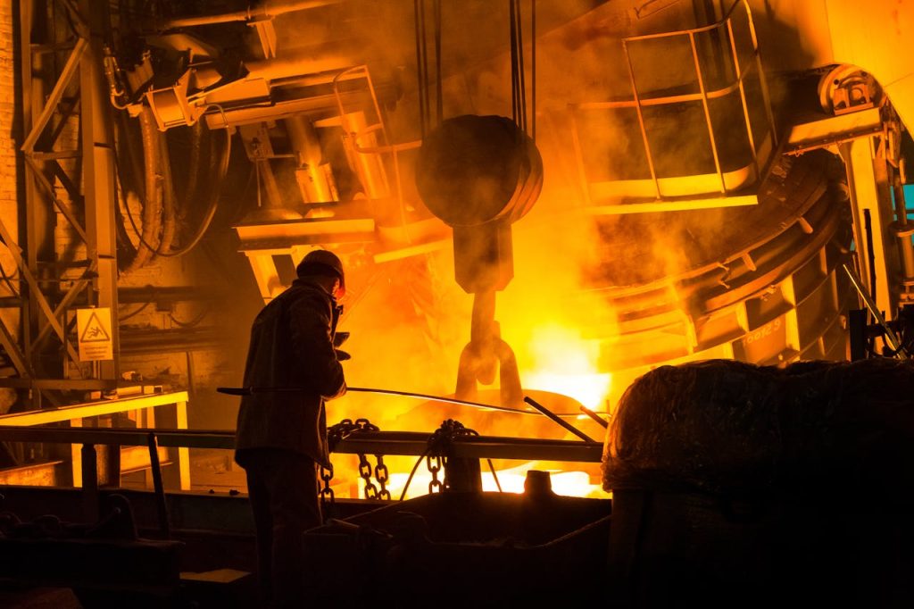 pexels photo 3361235 A worker operates machinery in a factory with molten metal and intense flames.